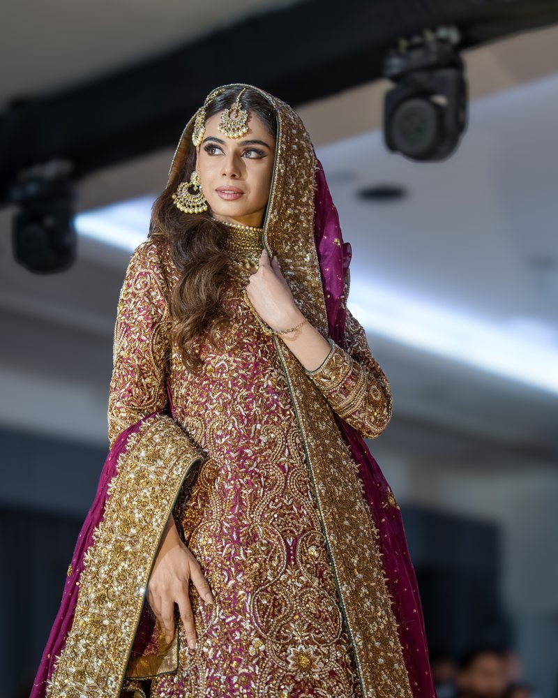 A model in a gold and magenta bridal outfit wearing a maang tikka, jhumkas and a layered choker