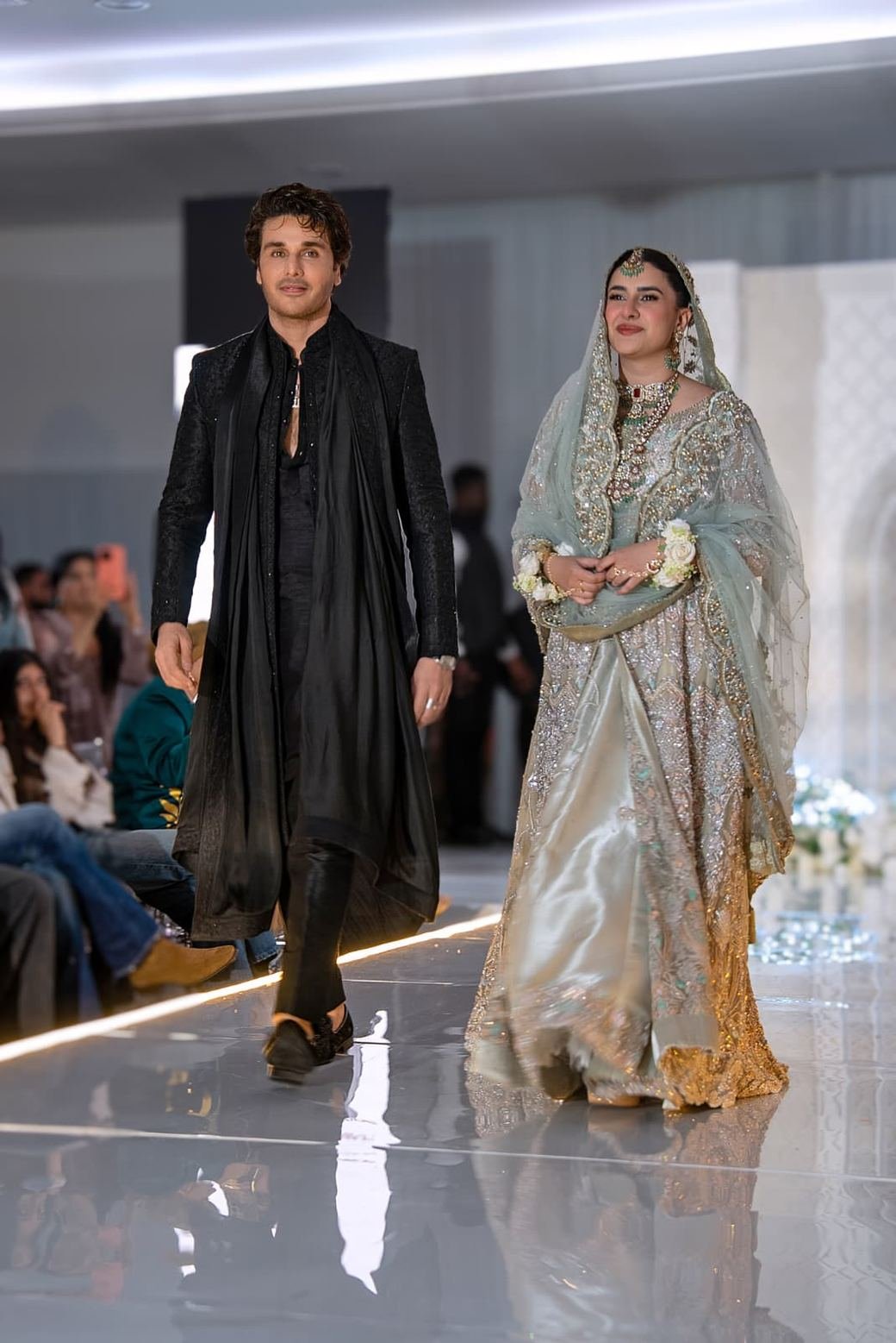 A couple walk the runway in bridal couture at Asian Bridal Fest UK — an embroidered
                    black sherwani and a pale gold lehenga with a beaded dupatta.